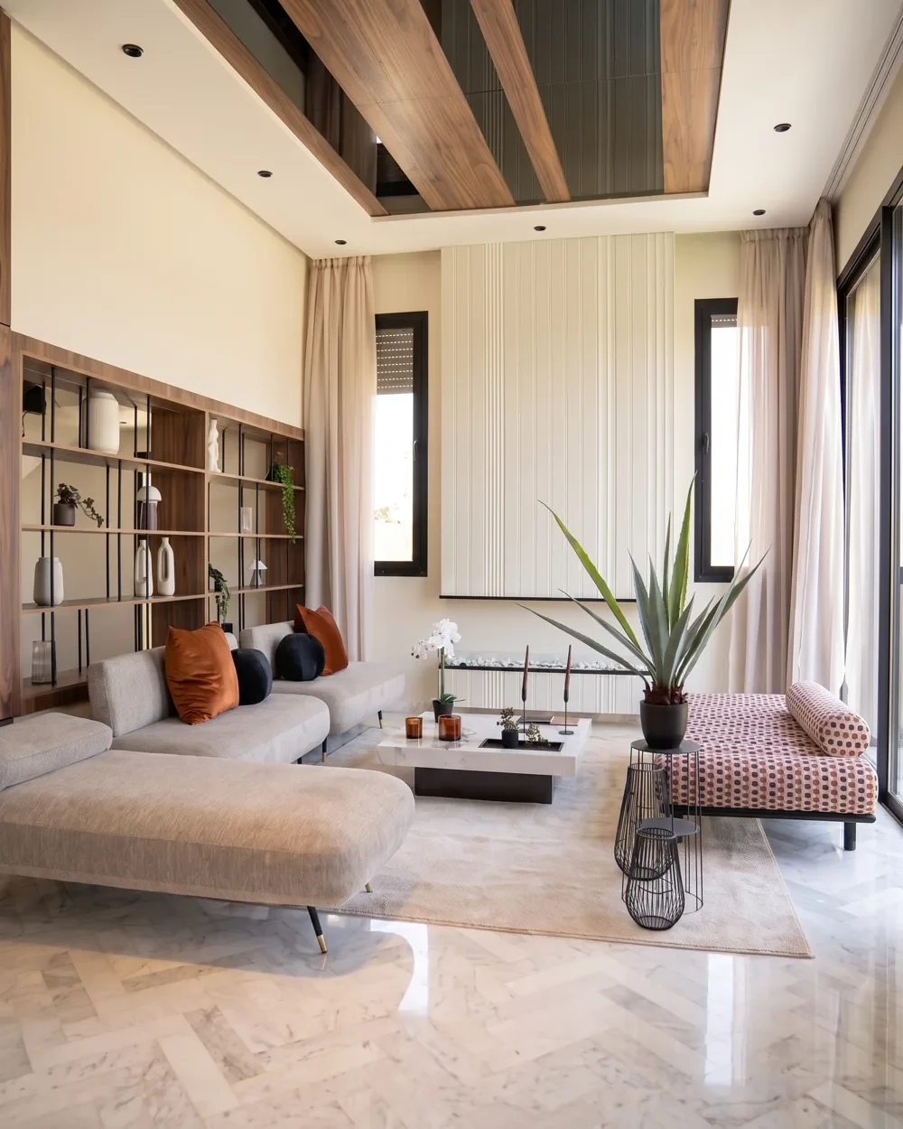 Le salon de la villa témoin — canapé d’angle gris clair et bibliothèque en noyer sous la double hauteur, photographié sur place