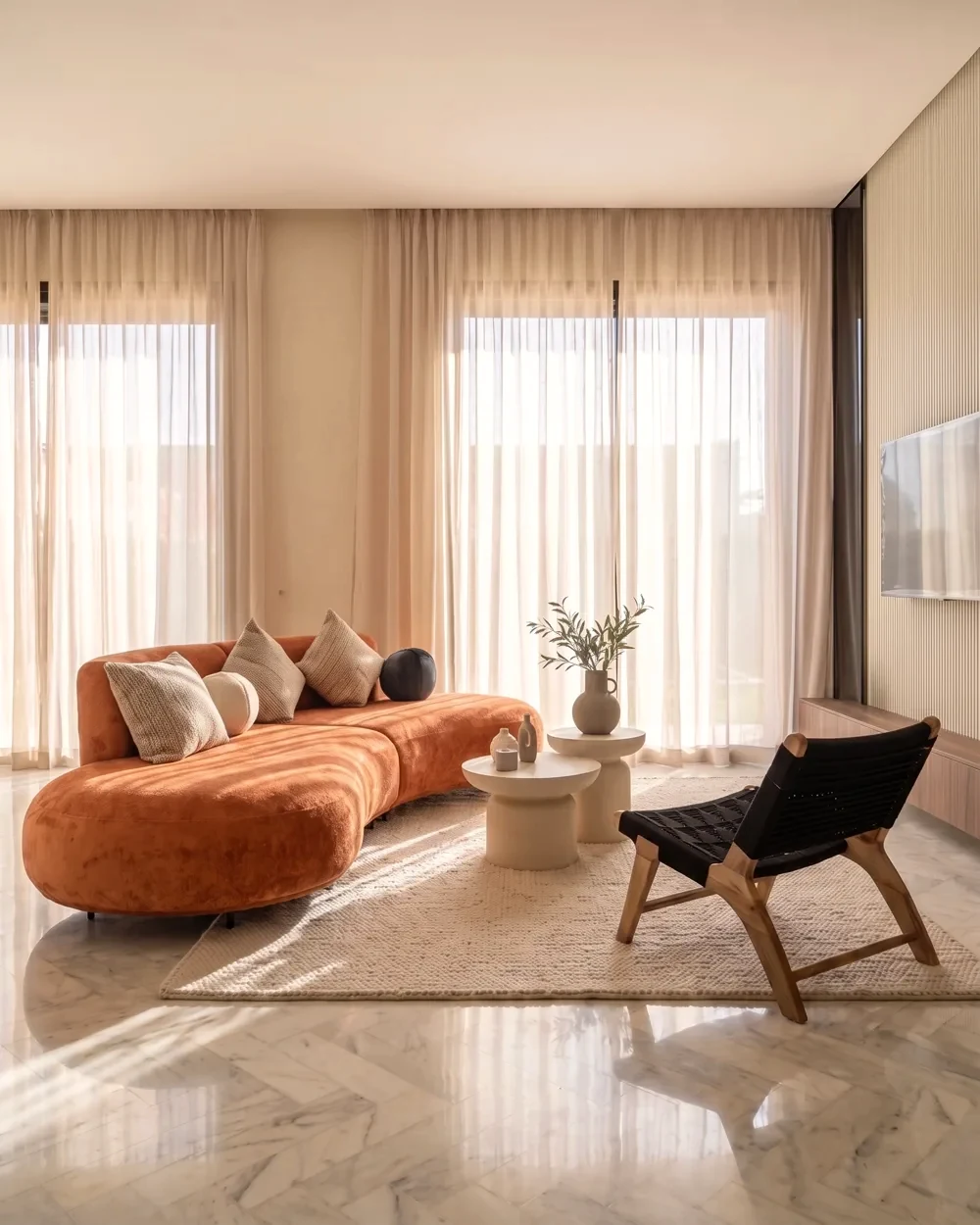 Le salon de la villa témoin — canapé galbé terracotta et voilages dans la lumière du matin, photographié sur place