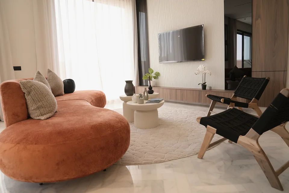 Le séjour de la villa témoin — mur média cannelé, sol en marbre et fauteuils en bois courbé, photographié sur place.