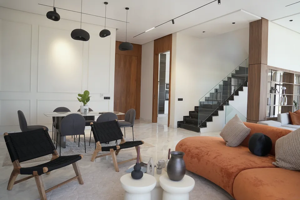 La salle à manger de la villa témoin — suspensions noires, menuiseries en noyer et escalier en pierre sombre, photographiée sur place.