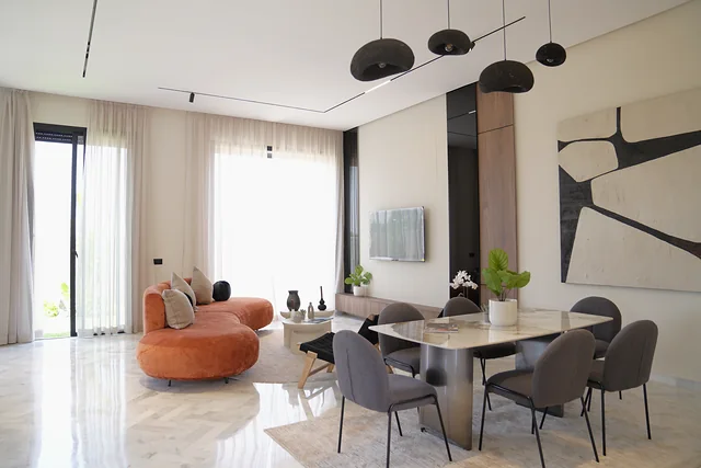 Le coin repas de la villa témoin : table de marbre, six chaises, suspensions sombres et grande toile abstraite sur le mur.