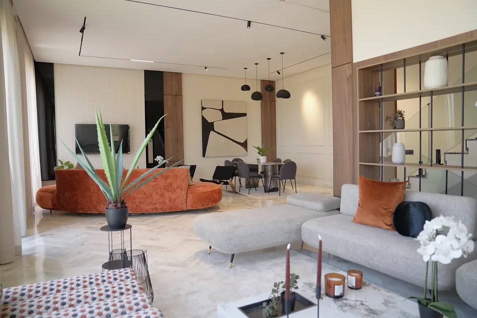 Séjour ouvert de la villa témoin Jnane Oum El Ghite — canapé galbé terracotta, banquette d’angle et bibliothèque en noyer, photographié sur place.